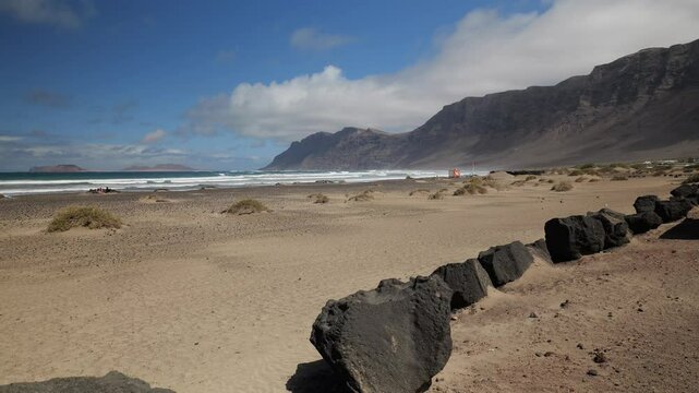 Volcanic rocks line famara beach with risco de famara cliffs in the background on lanzarote, canary islands