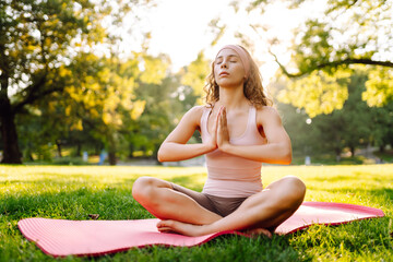 Morning yoga. Young beautiful woman  in sportswear stretching body on fitness mat at public park,...