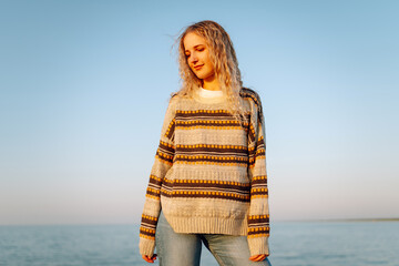 Young woman enjoying a breezy day at the beach near a vibrant red lighthouse at sunset. Travel,...