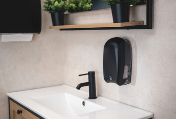 Black dispenser for electronic liquid soap and black dispenser for hand towels in a modern toilet.