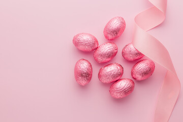 Chocolate easter eggs wrapped in pink colored foil on pink background. Top view.