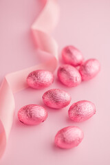 Chocolate easter eggs wrapped in pink colored foil on pink background.