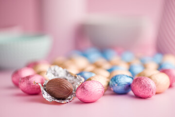 Chocolate easter eggs wrapped in multi colored foil on pink background.