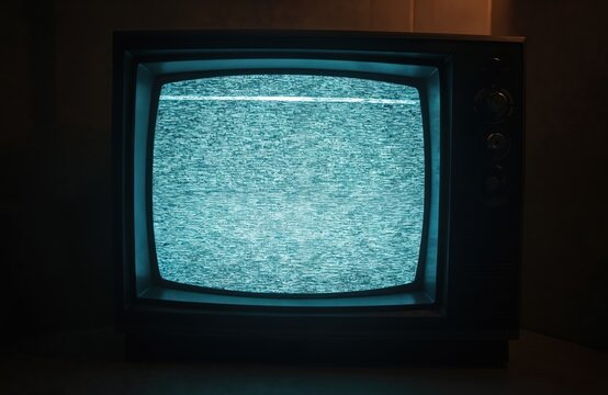 Old TV screen displays noisy image due to lack of signal. Black analog television with snow effect, shows broken broadcast, static waves. Grooved vintage tube TV in dark room.