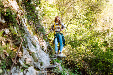 Obraz premium Woman tourist exploring nature in summer, walking across the bridge. Hiker with big backpack traveling in forests. Active lifestyle