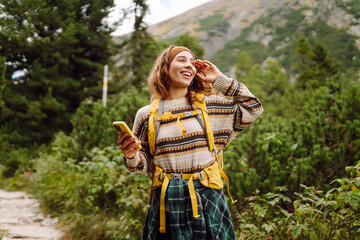 Smiling hiker using smartphone in forest.  Female tourist using mobile internet in woods. Blogging....