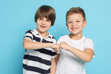 Cute brothers making fist bump on light blue background