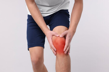 Young man suffering from pain in knee on light background, closeup