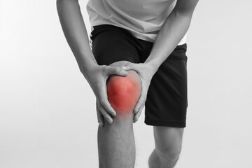 Young man suffering from pain in knee, closeup. Black-and-white effect with red color accent