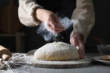 Woman sprinkling flour over dough at grey table, closeup