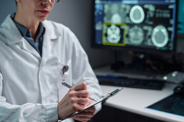 Scientist evaluating medical scans in laboratory. Wearing lab coat and using pen, the professional...