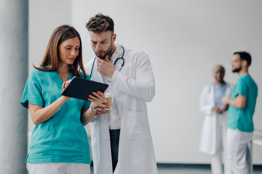 Doctors using digital tablet and discussing patient's medical history in hospital corridor