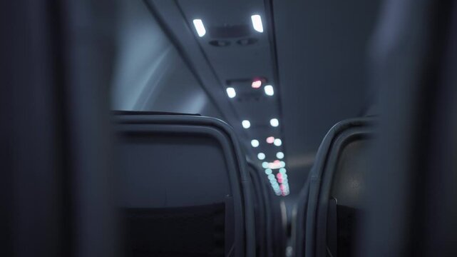 Quiet and empty airplane flight row of seats during nighttime with dimmed lights. Flying at night with darkened lights. Seen from plane seat down the aisle. Almost no passengers on board flight