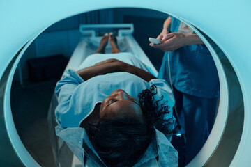 Medical professional monitoring African American patient during MRI scan session, ensuring accurate...