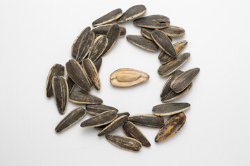 Sunflower seeds arranged in circle on white background showing one open seed