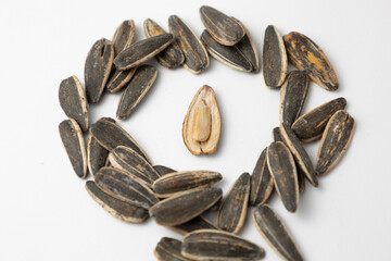 Sunflower seeds forming a circle around a single peeled seed on white background