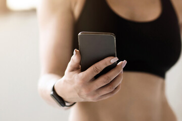 Slim body, fit model, trainer in middle age and modern technology. Muscular mature female in sportswear with fitness tracker looking at smartphone and reads message or sports blog, cropped, free space