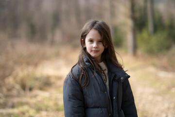 A girl facing the camera wearing a jacket outside on a path in the forest. Concept of children's leisure and emotions