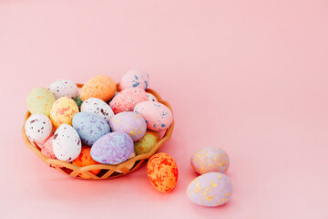 Colorful Easter eggs are placed in a woven basket on a soft pink background, exuding festive cheer.