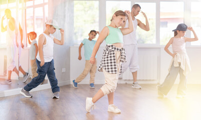 Fototapeta premium Emotional tween girl dancer rehearsing modern krump dance moves during group workout in kids studio under guidance of male instructor