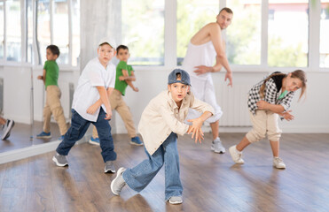 In sports studio, creative childrens team learns hip-hop dance accompanied by experienced man teacher