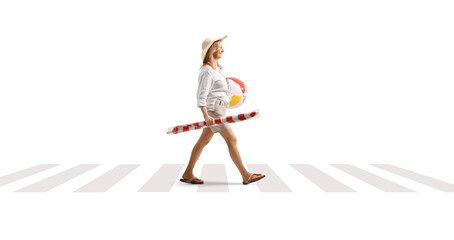 Woman carrying a beach ball and umbrella and walking at pedestrian crossing