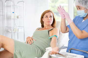 Fototapeta premium Anesthesiologist doctor injecting pain medication into vein of woman before starting surgery in a cosmetology clinic