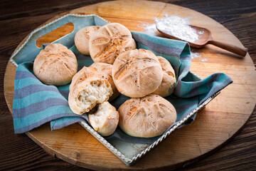Freshly baked Kaiser rolls offered as close-up on a rustic wooden tray