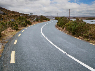 Dangerous narrow Irish country road with white no overtake line in a rural area. Cloudy sky. Nobody. Road safety concept. High quality asphalt surface.