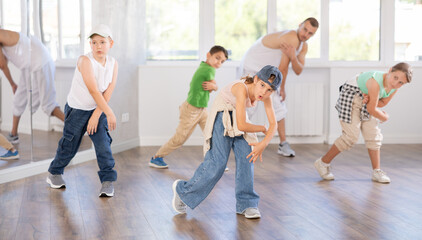 Positive teen boys and girls dancing modern street dance together during their group training at light dance hall