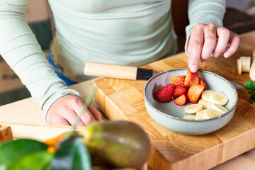 Girl eating strawberry from the bowl, healthy eating concept in the kitchen.