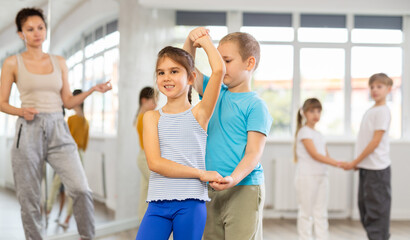 Happy preteen children practicing ballroom dances in pairs in training hall during dancing classes
