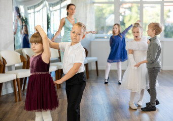 Enthusiastic preteen children, boys and girls in party attire performing elegant waltz in pairs in...