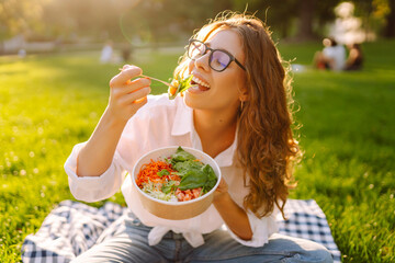 Woman eating healthy meal sitting on blanket in sunny park. Healthy food plate. Vegetarian