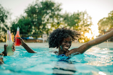 Young woman holding drinks, enjoying summer pool party with friends