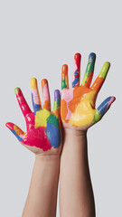 Two child's hands, palms up, covered in multicolored paint, against a light gray background, showcasing creativity and childhood innocence