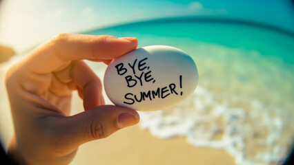 Hand gripping minimalist white stone with bye bye summer text against turquoise waters and pristine sandy shoreline