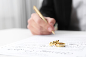 Man signing marriage contract and wedding rings on desk, selective focus