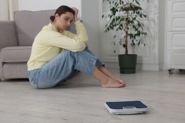 Depressed woman and scales on floor at home, selective focus. Bulimia problem