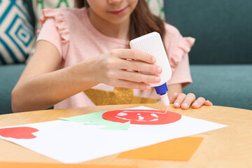 Girl applying glue onto paper figure for her creative project at table indoors, closeup. Art and craft