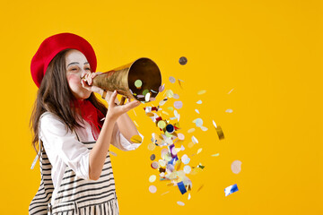 Happy girl dressed like mime with megaphone and confetti on yellow background, space for text....