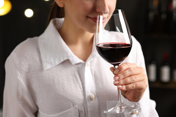 Professional sommelier tasting red wine in glass indoors, closeup