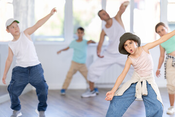 Obraz premium Portrait of cheerful girl and group of active children practicing hip-hop dance in light dance hall