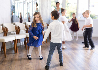 Obraz premium Cheerful preteen girl in blue lace dress dancing twist with classmates in bright classroom, full of energy and joy during school party ..