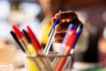 Extreme close up of pen taken by person from desk organizer to annotate document. Focus on workspace stationary holder used by student in blurry background requiring writing tool