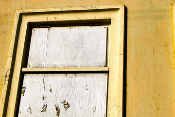 a weathered and worn yellow boarded up window with white plywood, likely for protection or security. architectural background. 