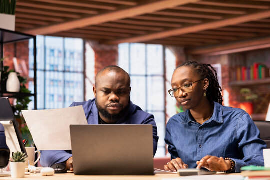 African American couple reviews their taxes and finances at home, using a calculator and laptop to track expenses, manage bills and plan their budget at home office. Financial responsibility. - Powered by Adobe