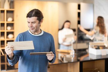 Mature man stands in a furniture store and looks at wood samples for a kitchen set, he chooses a...