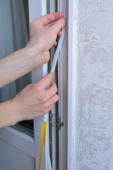 A man's hands insulates windows and balcony doors with foam adhesive tape. Close up. Budget renovation in the apartment. Preparation for the cold snap. Heating problem in apartment buildings