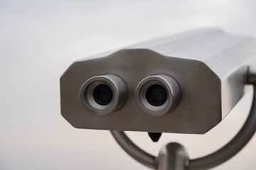 Metallic binocular with blurred background under overcast sky. Closeup of outdoor coin operated binocular viewer for tourists. Telescope, observation, exploration, discovery, travel and nature concept
